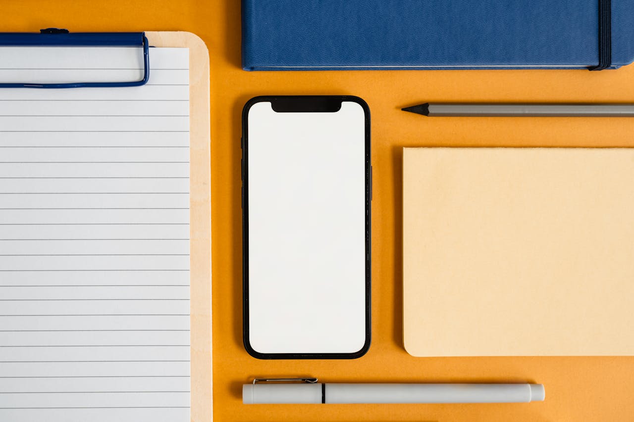 A flat lay of office supplies with a smartphone on a yellow surface, perfect for business and productivity themes.